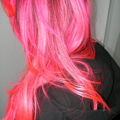 Side view of long wavy hair with neon pink ends and black roots, professional hair coloring at Assort London.