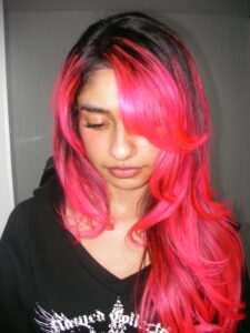 Close-up of vibrant flamingo pink hair with natural dark shadow roots, high-contrast hair color trend 2026.